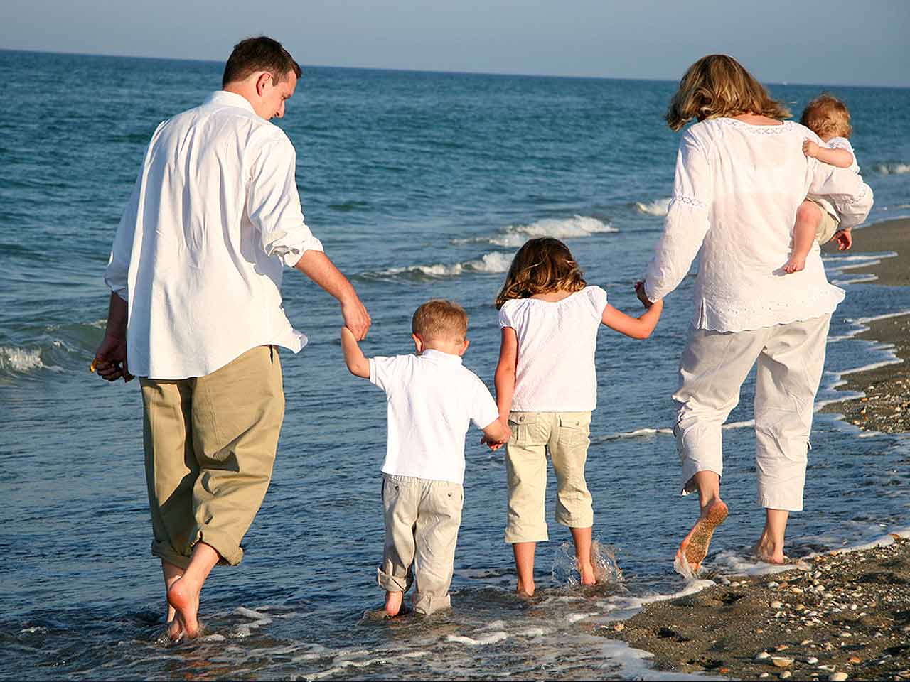 Familj går längs med stranden och håller varandra i hand