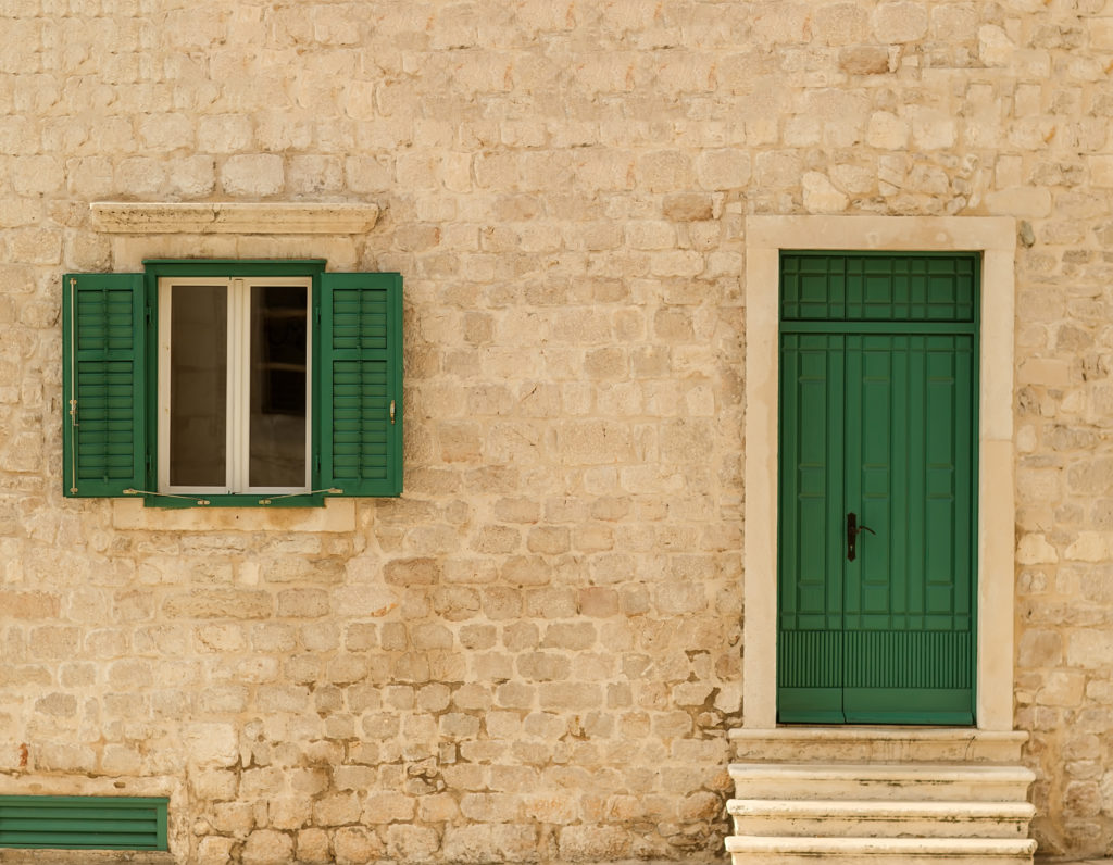 Photo closeup of old aged building made of beige stone masonry with green wooden door and shutters open window outside on cityscape background horizontal picture