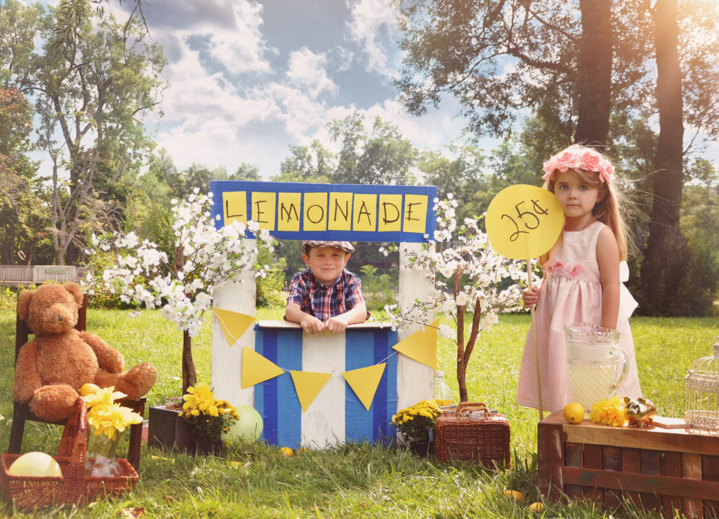 Two little kids are selling lemonade at a homemade lemonade stand on a sunny day with a price sign for an entrepreneur concept